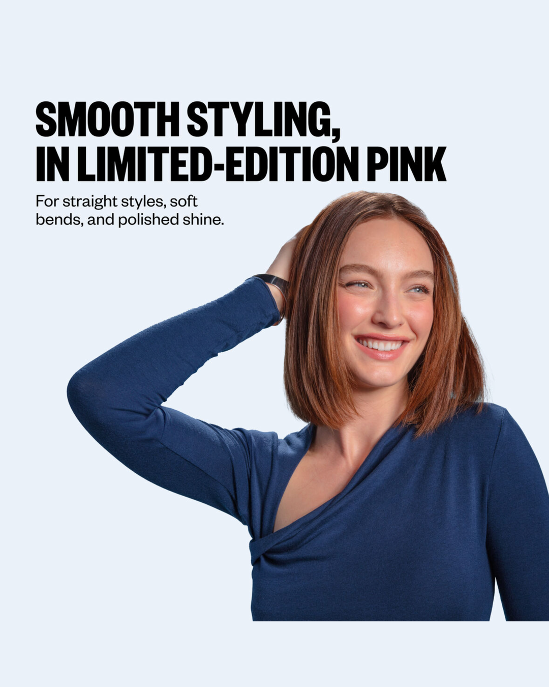 A smiling woman with shoulder-length auburn hair wears a navy long-sleeve wrap-style top against a very light blue background. Large black text at the top reads, 'SMOOTH STYLING, IN LIMITED-EDITION PINK.